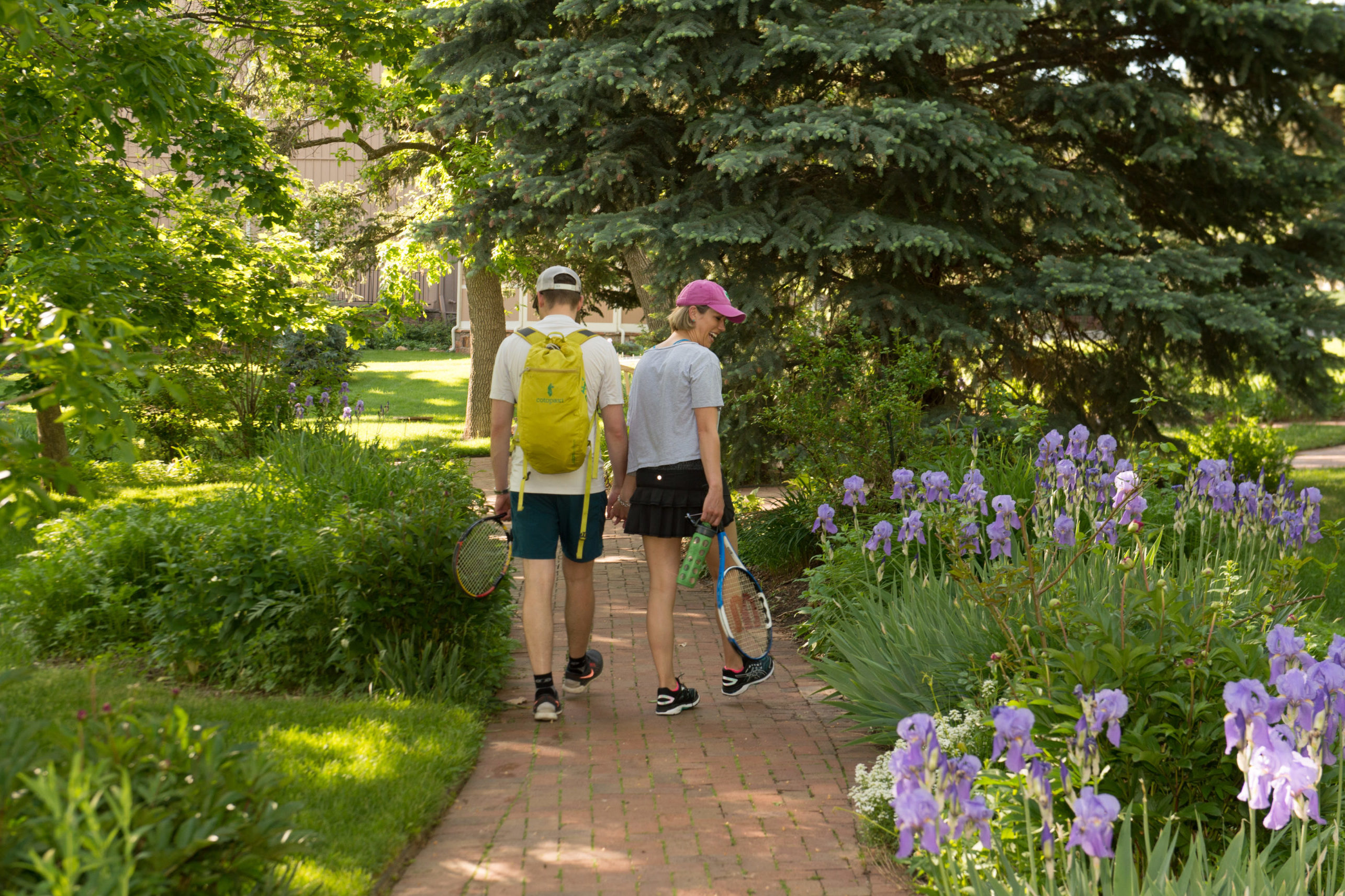 Couple walking through gardens with tennis racquets