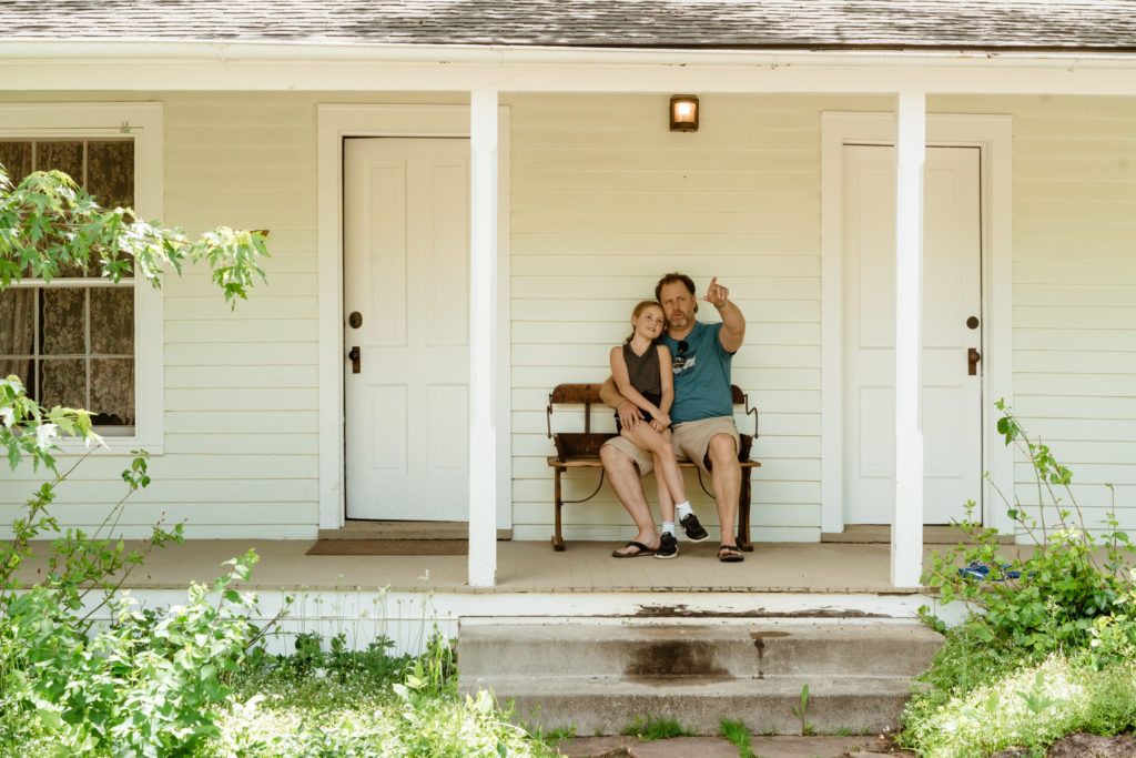 Daughter and father sitting on bench on cottage porch. Father pointing at something