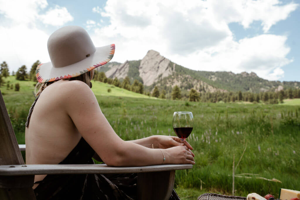Woman with glass of wine sitting in chair and looking at Flatirons mountains